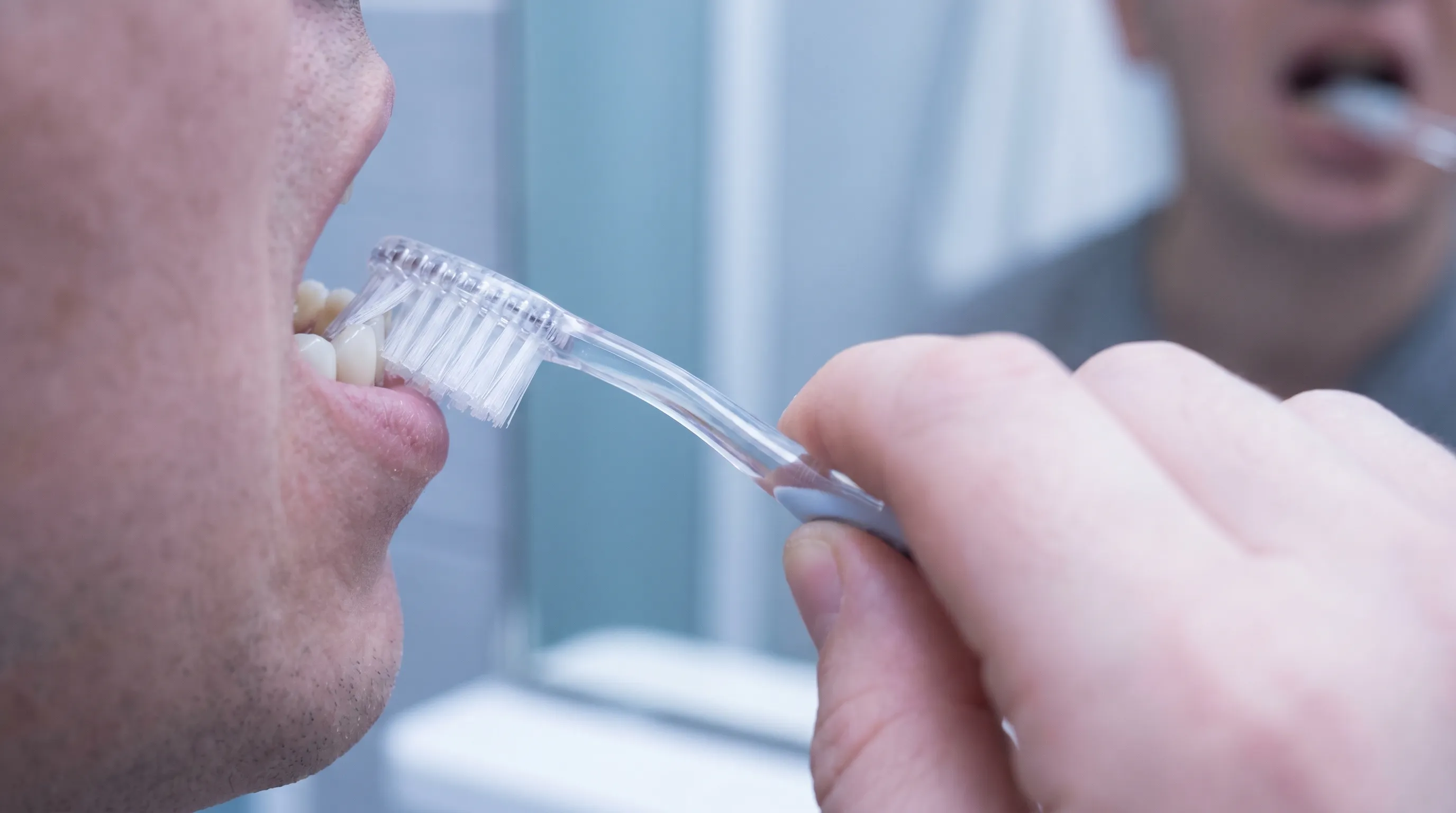 A close-up of a patient gently brushing their teeth with a soft-bristle toothbrush, focusing on gentle oral hygiene technique around a dental restoration, soft blue and gray tones, medical lifestyle photography, 4:3 ratio
