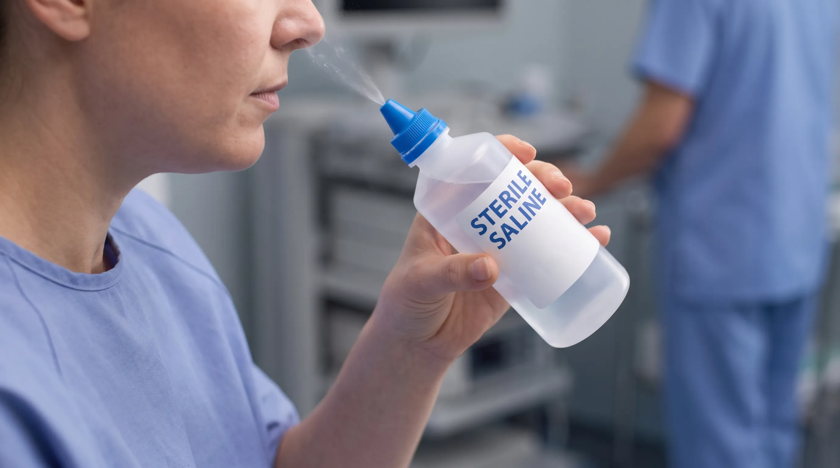Close-up of a patient using a sterile saline nasal spray bottle for sinus relief