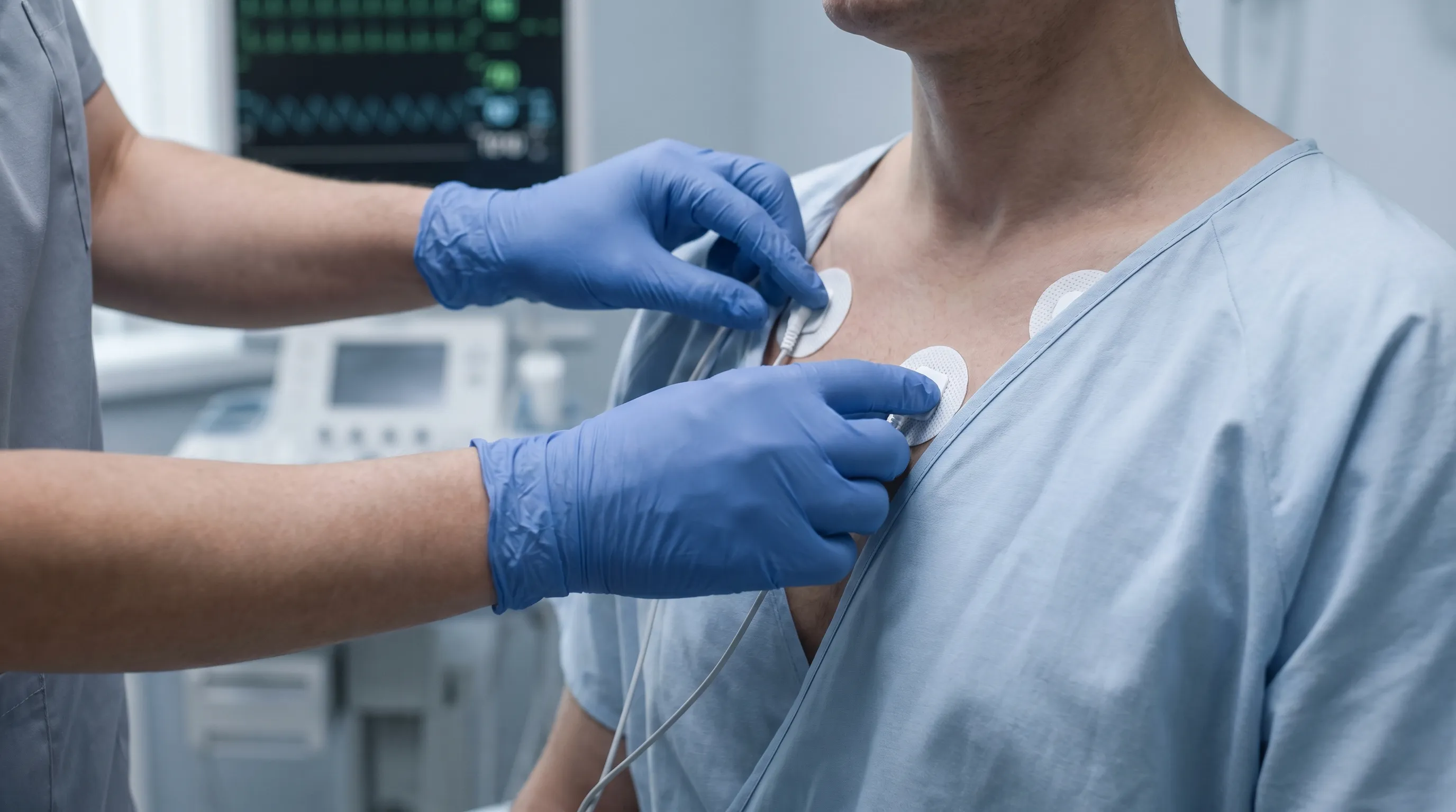 Close-up view of a healthcare technician carefully placing adhesive ECG electrode pads on a patient's chest in a bright clinical examination room