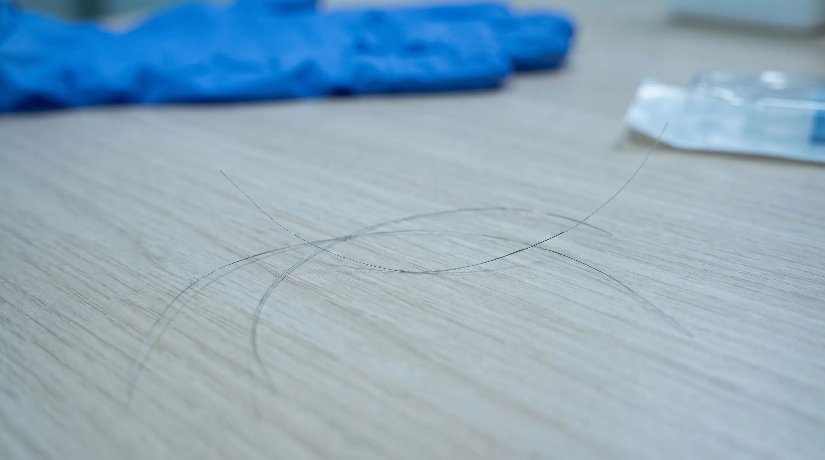Close-up clinical photograph showing a few strands of shed hair resting on a clean wooden surface, emphasizing the natural progression of post-operative shedding, soft lighting, gray and blue tones