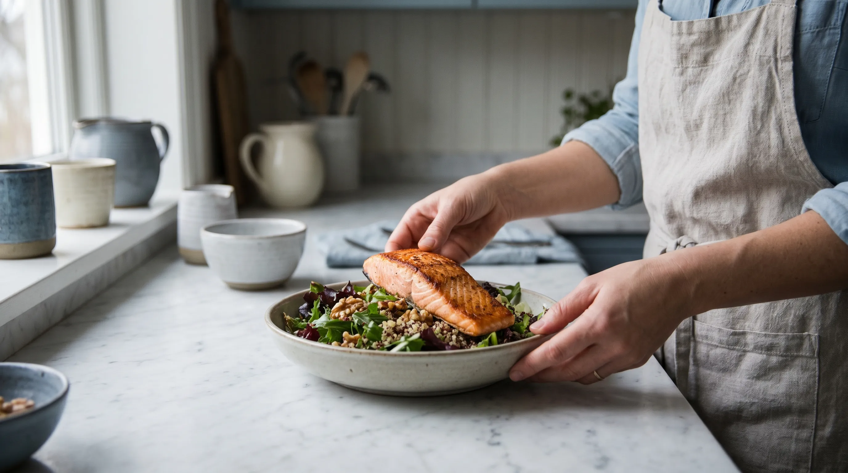 Person preparing a protein-rich meal with salmon, leafy greens, and nuts on a marble countertop, focusing on dietary recovery, soft lighting, gray and blue tones