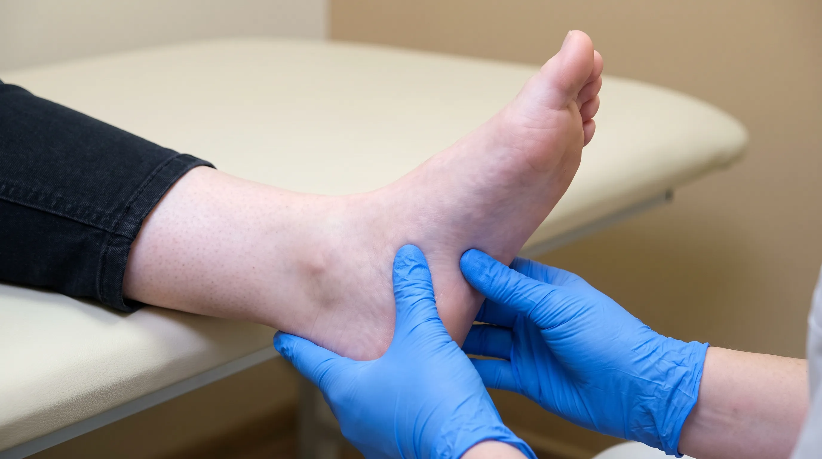 Close-up of a healthcare professional's hands gently palpating the arch area of a patient's foot, neutral clinical background, medical photography style