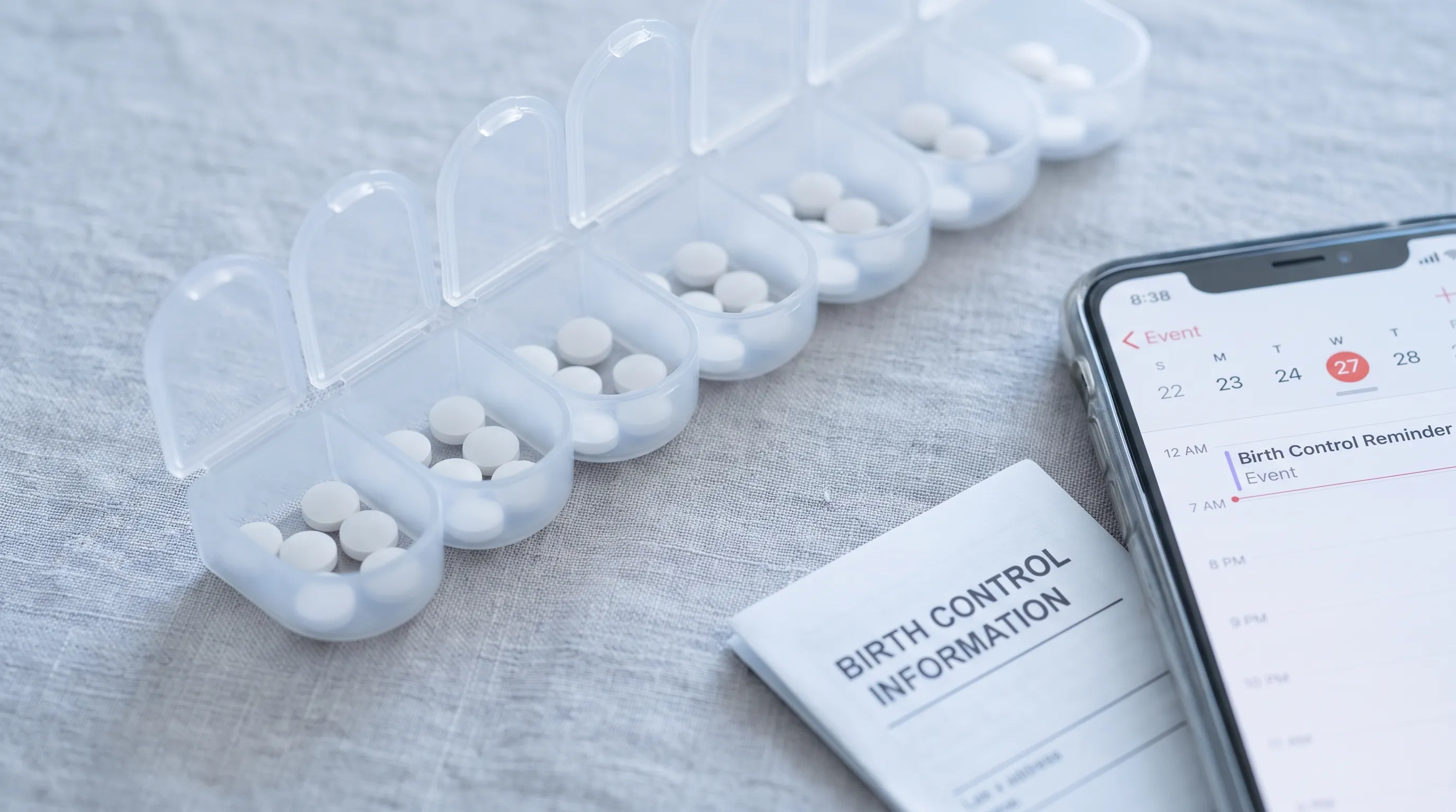 Close-up of birth control pill organizer next to medical calendar